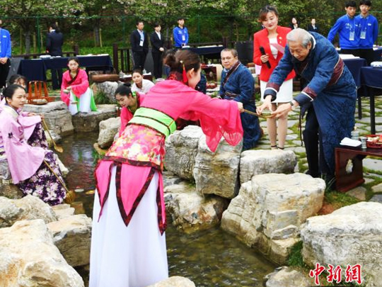 來自海內(nèi)外的書法家身著晉服，在曲水邊品酒、賦詩、揮毫。